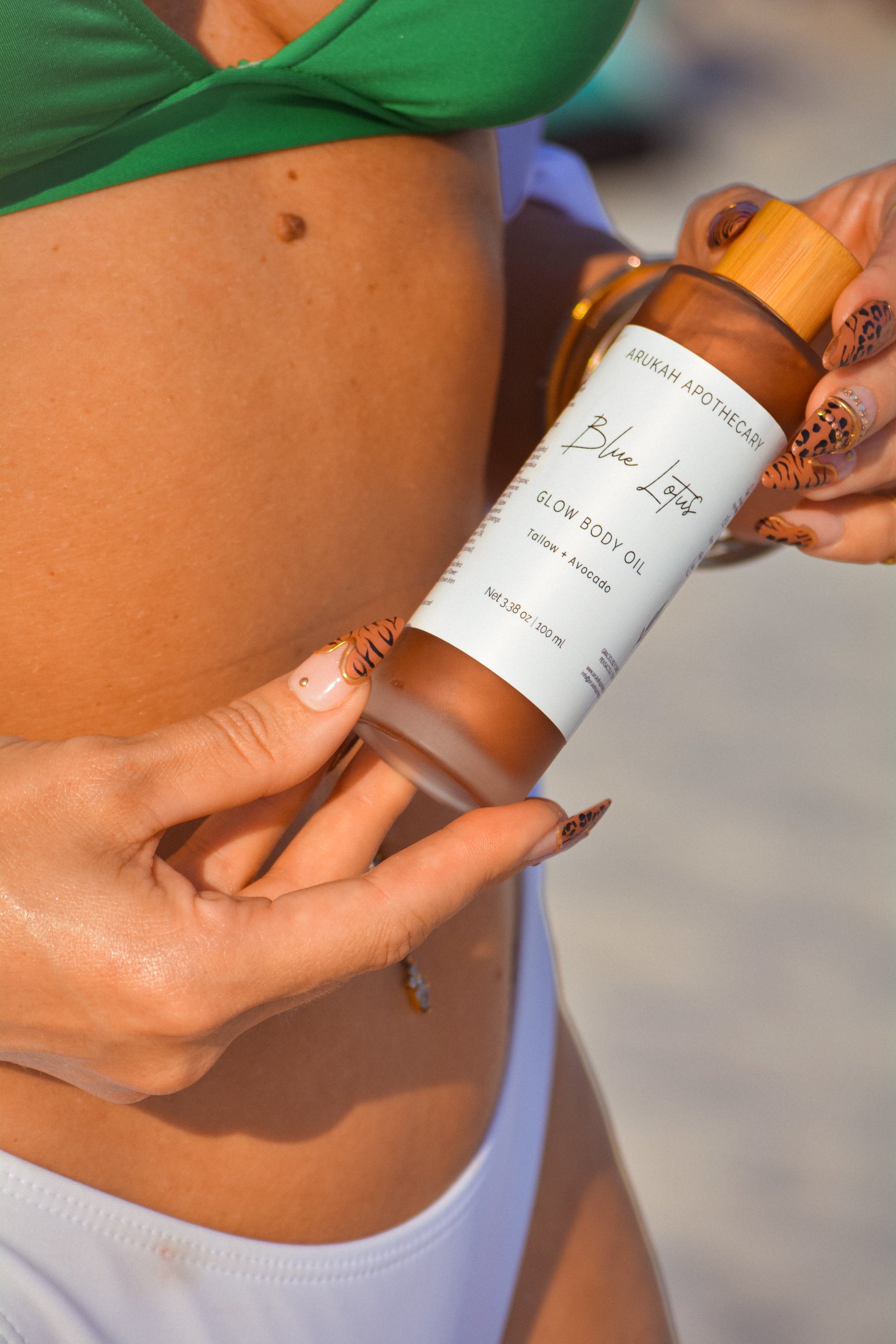 Blue Lotus Glow Body Oil held by model in green bikini